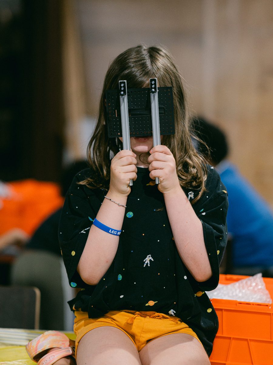 A BeanBots student holds up a piece of the robot frame in front of her face