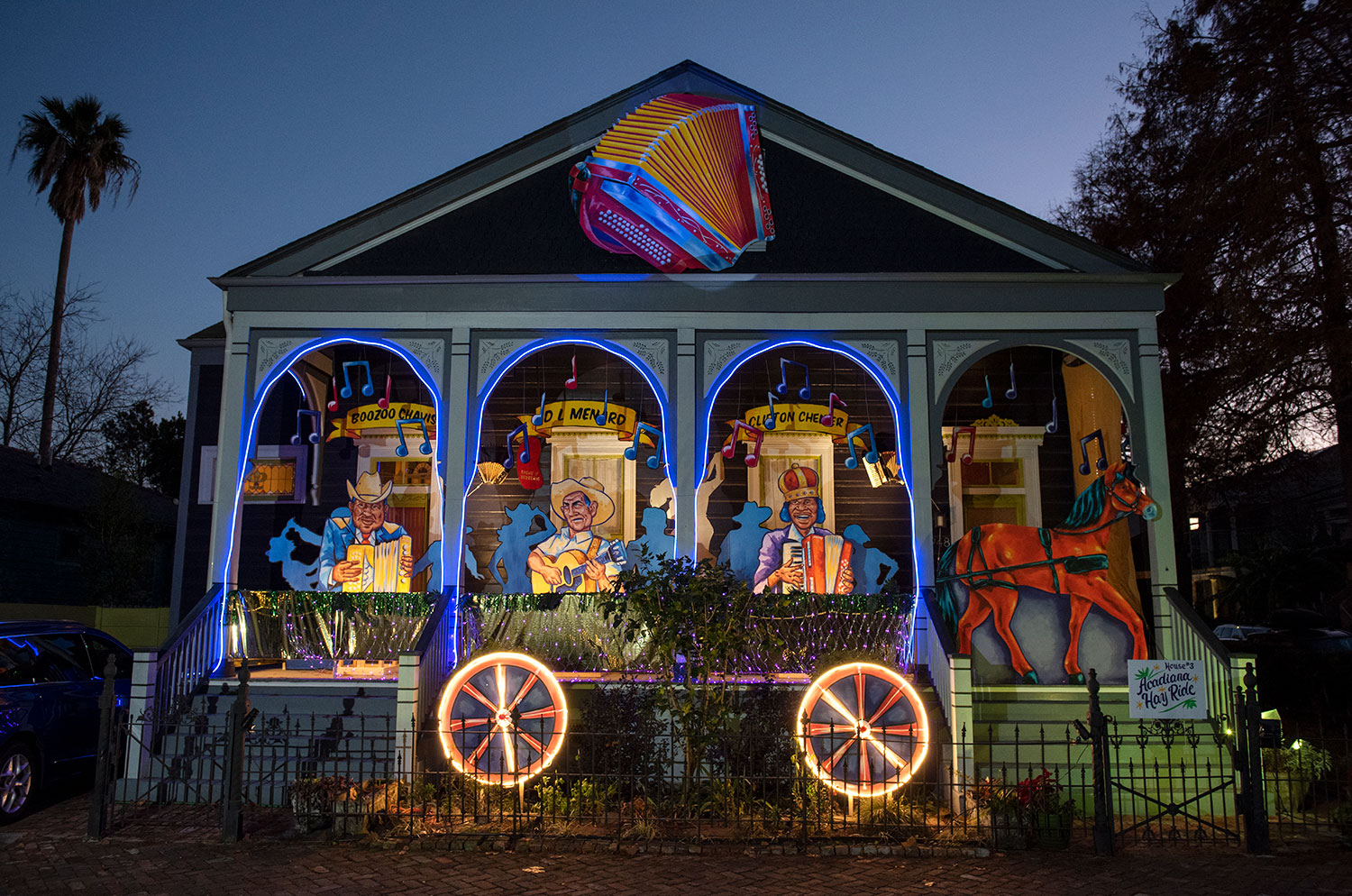 Acadiana Hay Ride house float lit up at night — Boozoo Chavis, D.L. Menard, and Clifton Chenier in neon blue arches